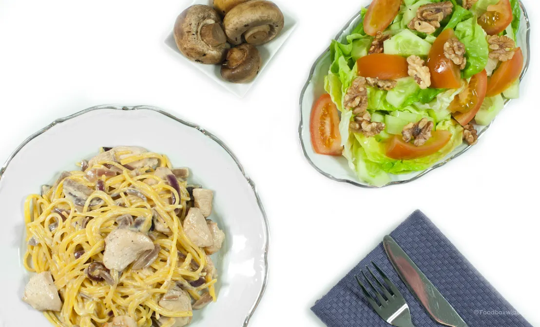 Een bord met spaghetti een kip-roomsaus en daarnaast salade en champions