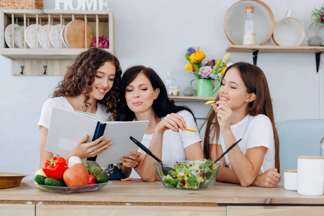 Drie vrouwen in de keuken bekijken het recept dat ze gaan klaarmaken