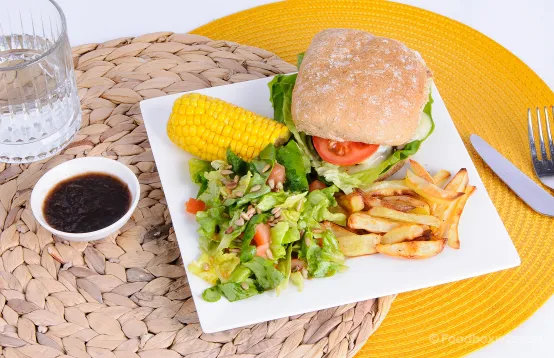 Op het bord een mix van veel kleuren met een vegan burger, salade, maiskolf en zelfgemaakte frietjes