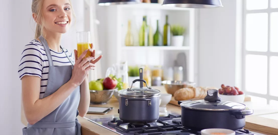 Vrouw staat in de keuken met een glas sinaasappelsap in de hand terwijl ze aan het koken is