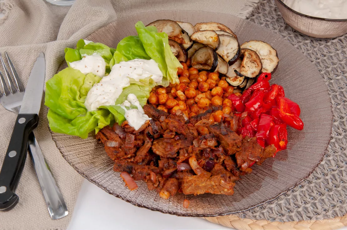 Een vegetarisch gerecht van green chef met kikkererwten en veel geroosterde groenten en sla op een glazen bord met een servet ernaast