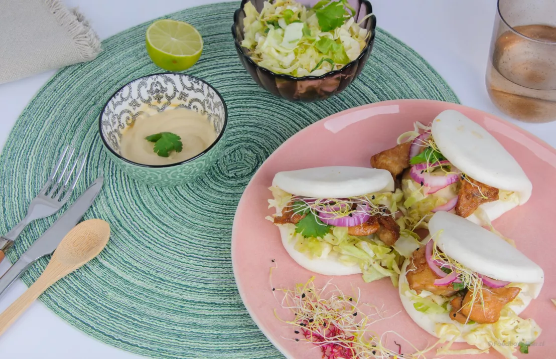 Op een roze bord liggen bao buns geserveerd met kippenvlees en koolsalade van een recept van crisp