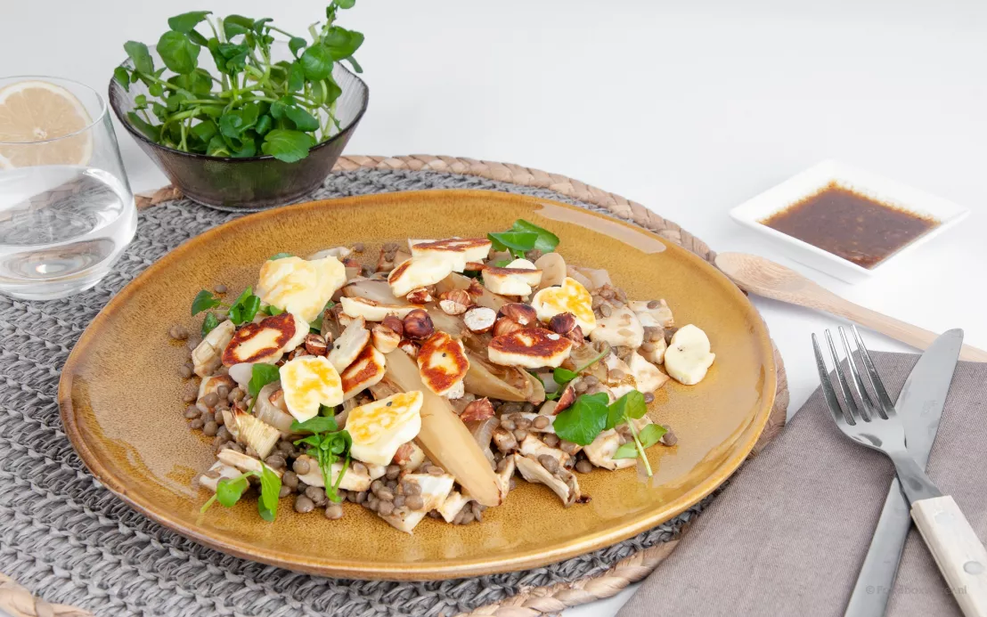 Op een geel bord een heerlijke salade van witlof, linzen, hazelnoten en grillkaas met verfrissende smaken.