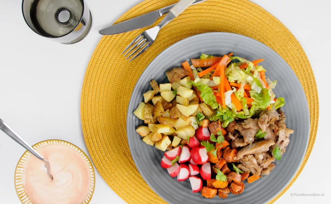 Op een blauw bord met placemat eronder een gerecht van crisp weekbox met shoarma en veel groenten